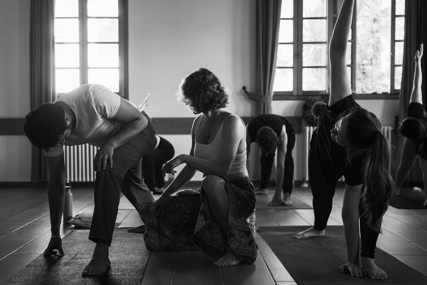 Vuxna utövar yogaövningar på mattor i en solig studio.