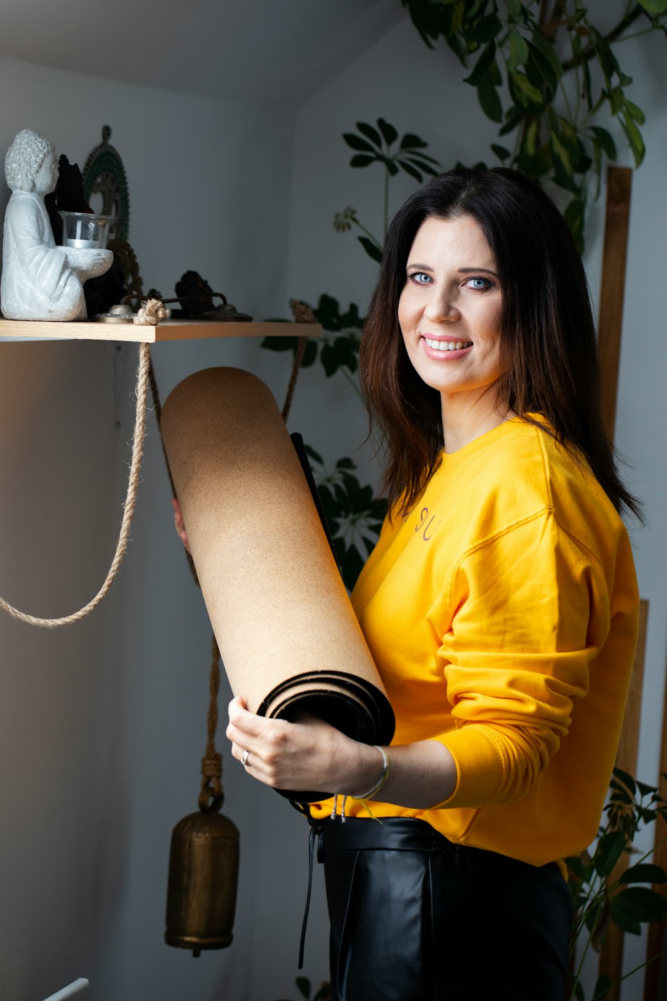 Kvinna i gul sweatshirt håller en yogamatta inomhus.