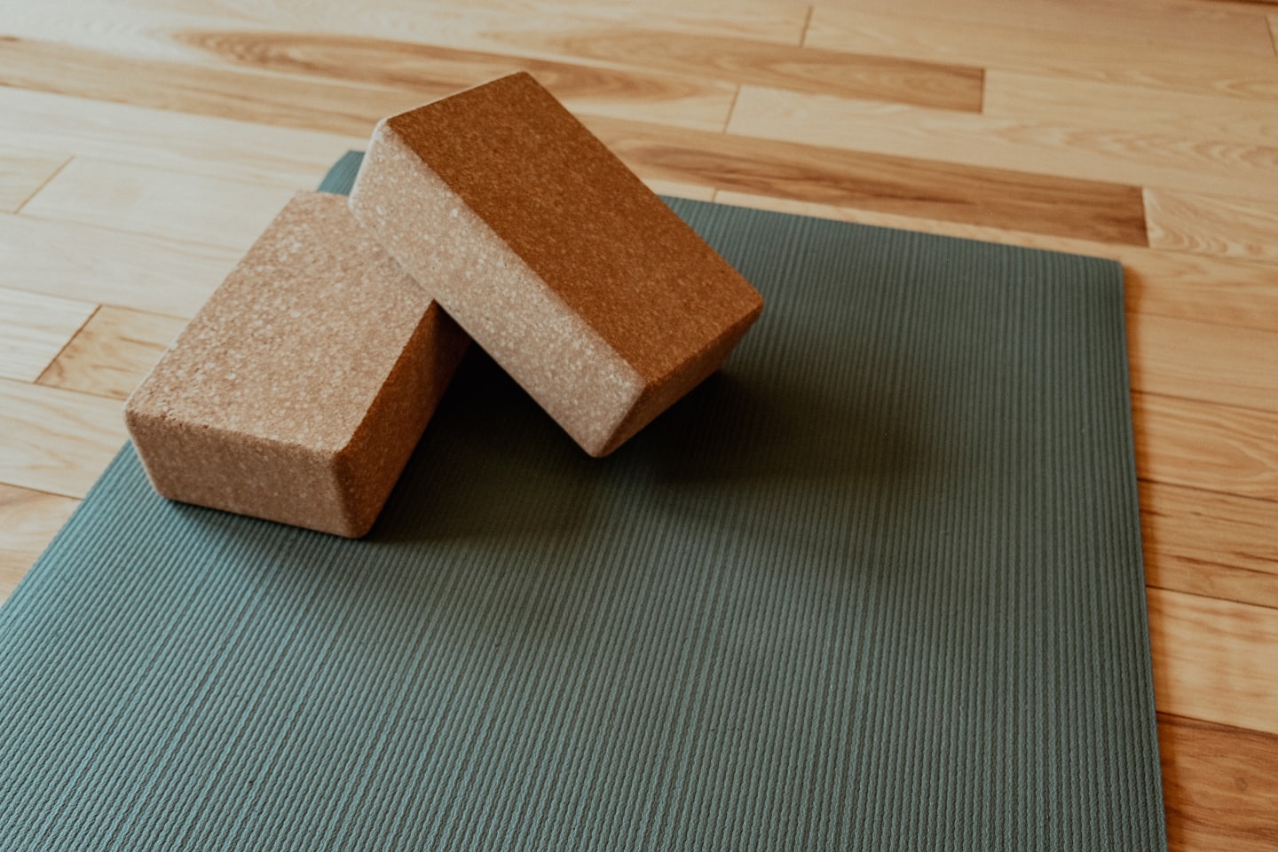 Två yogablock i kork ligger på en mörkgrön matta.